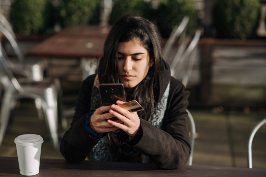 A woman holding a credit card is looking at her phone.