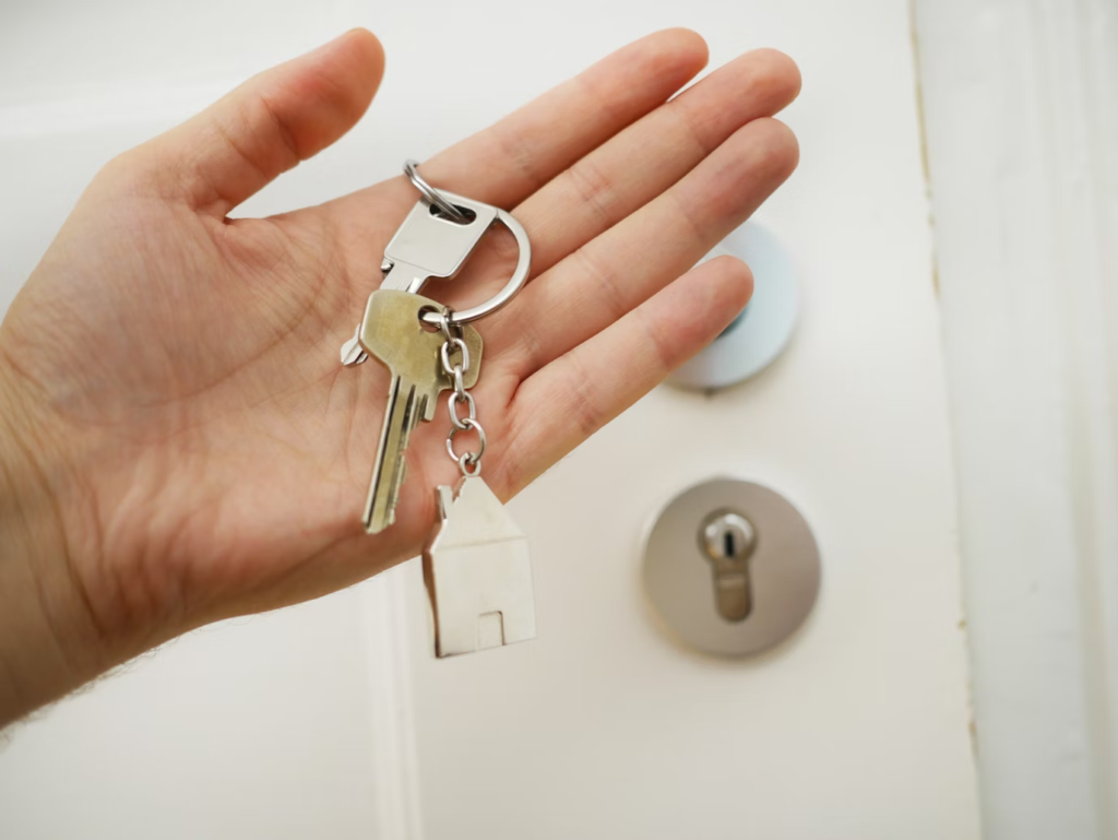 A hand holding keys with house shaped key chain.