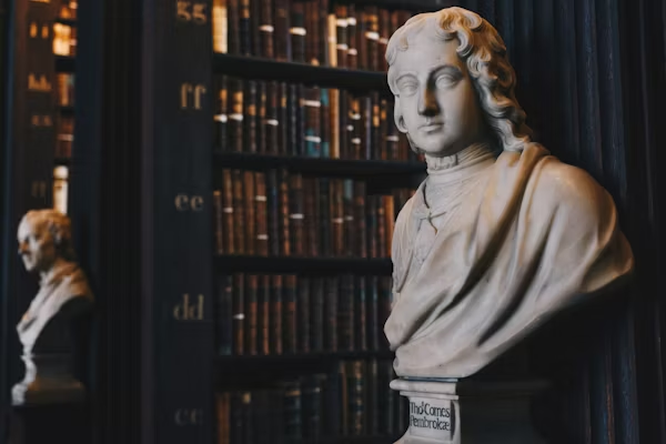 A bust of a woman in front of some books.