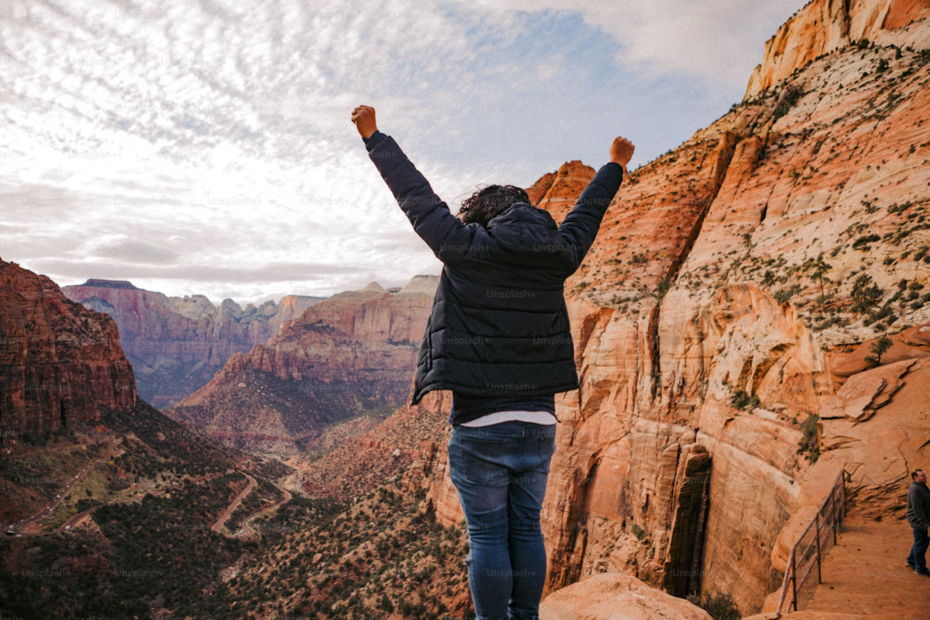 A person standing on top of a mountain with their hands in the air.