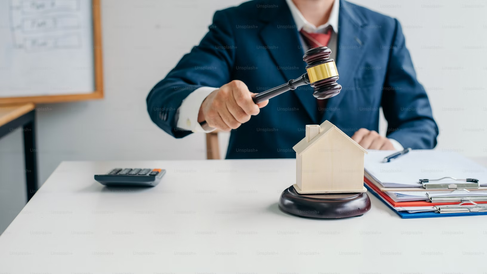 A man in suit and tie holding a gavel over a small house.