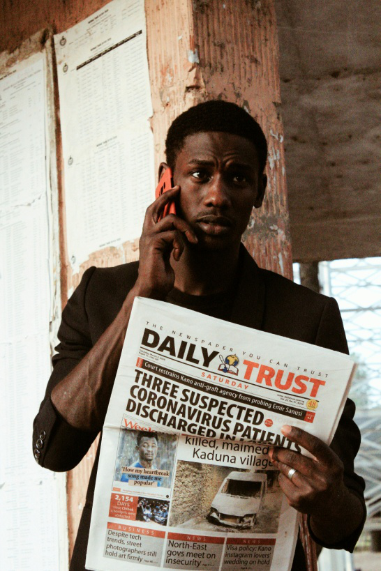 A man holding up a newspaper while talking on the phone.