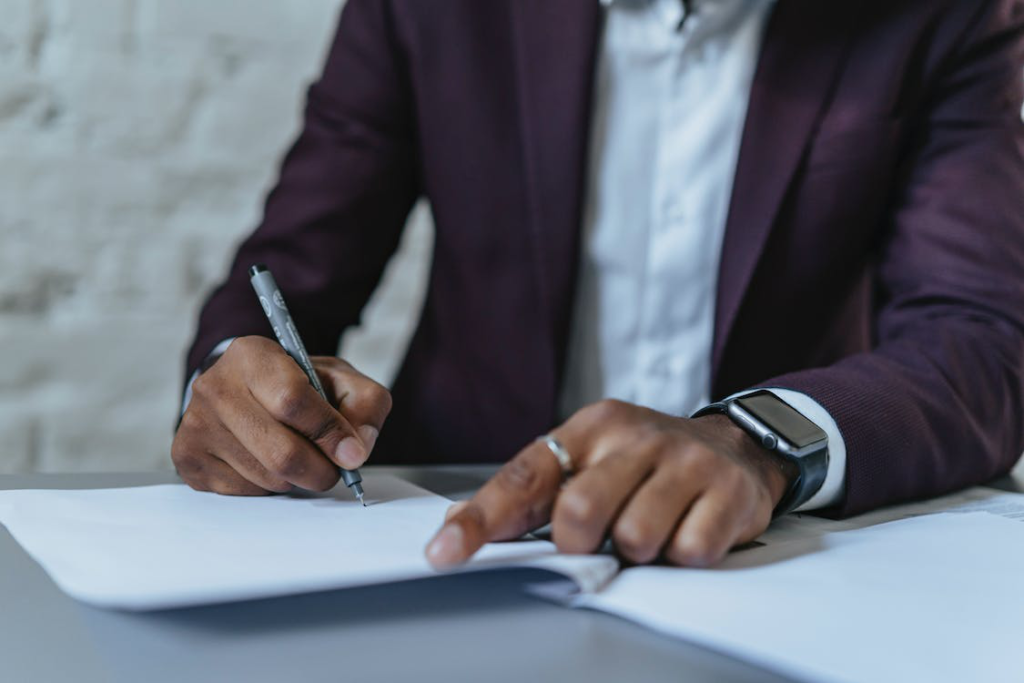 A man in a suit writing on paper with a pen.