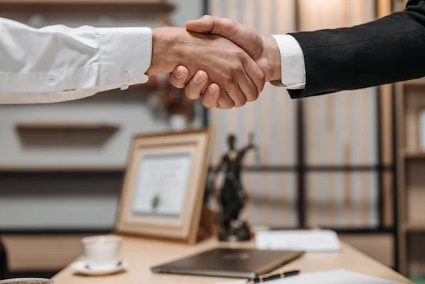 A lawyer and a client shaking hands in an office after discussing a debt relief strategy.