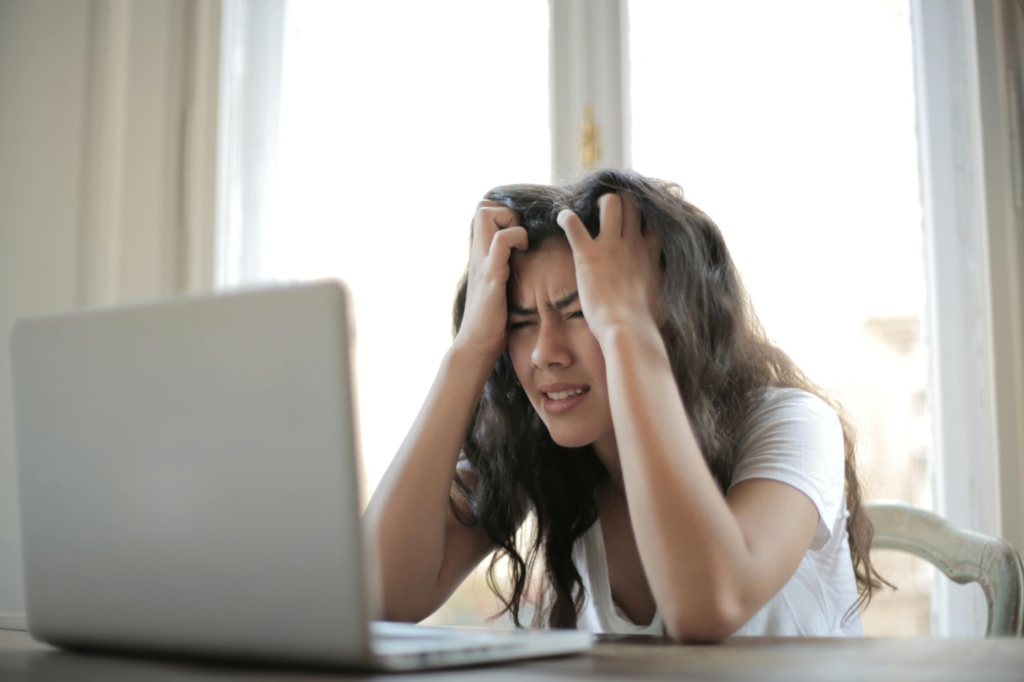 A distressed woman holding her head while looking at the laptop screen