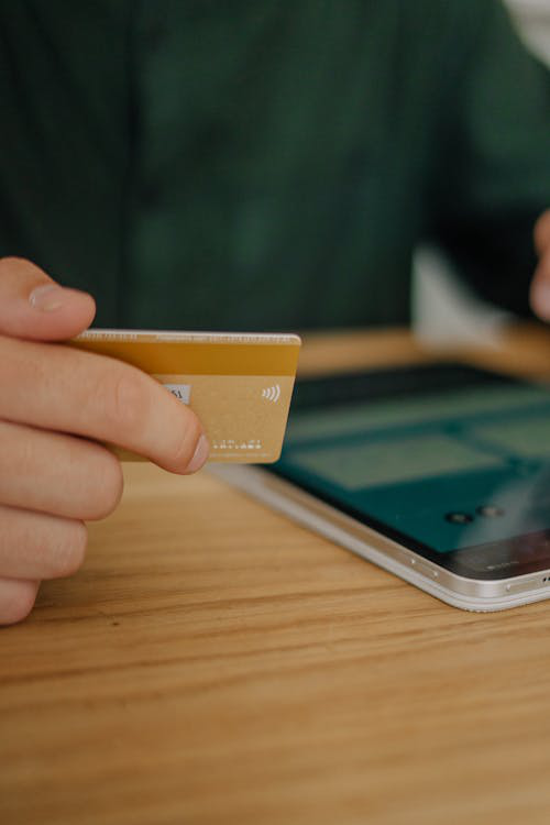 A close-up of a person holding a credit card in one hand and using a digital tablet with the other.