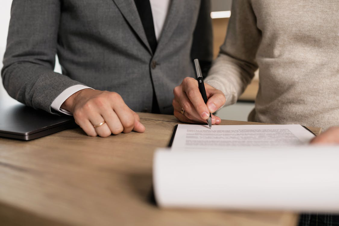 A person holding a pen and signing a printed contract document on a clipboard.