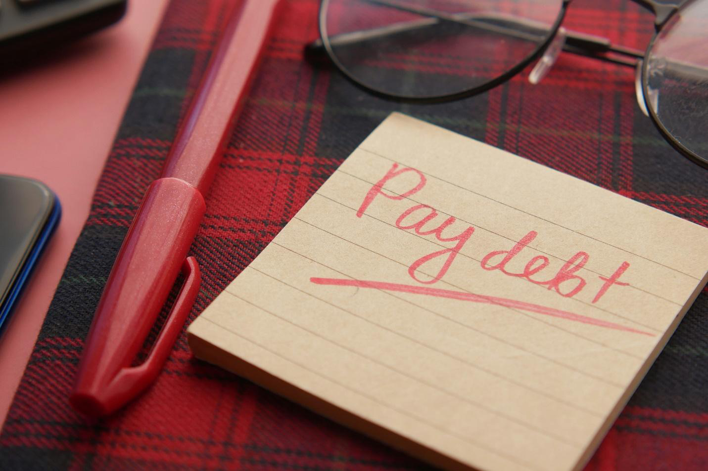 a pen, a sticky note with ‘pay debt’ written on it and glasses