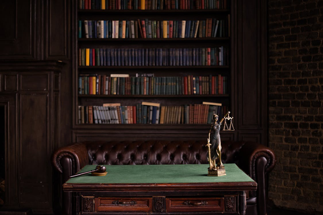 Lady Justice statue in front of a bookshelf on a table