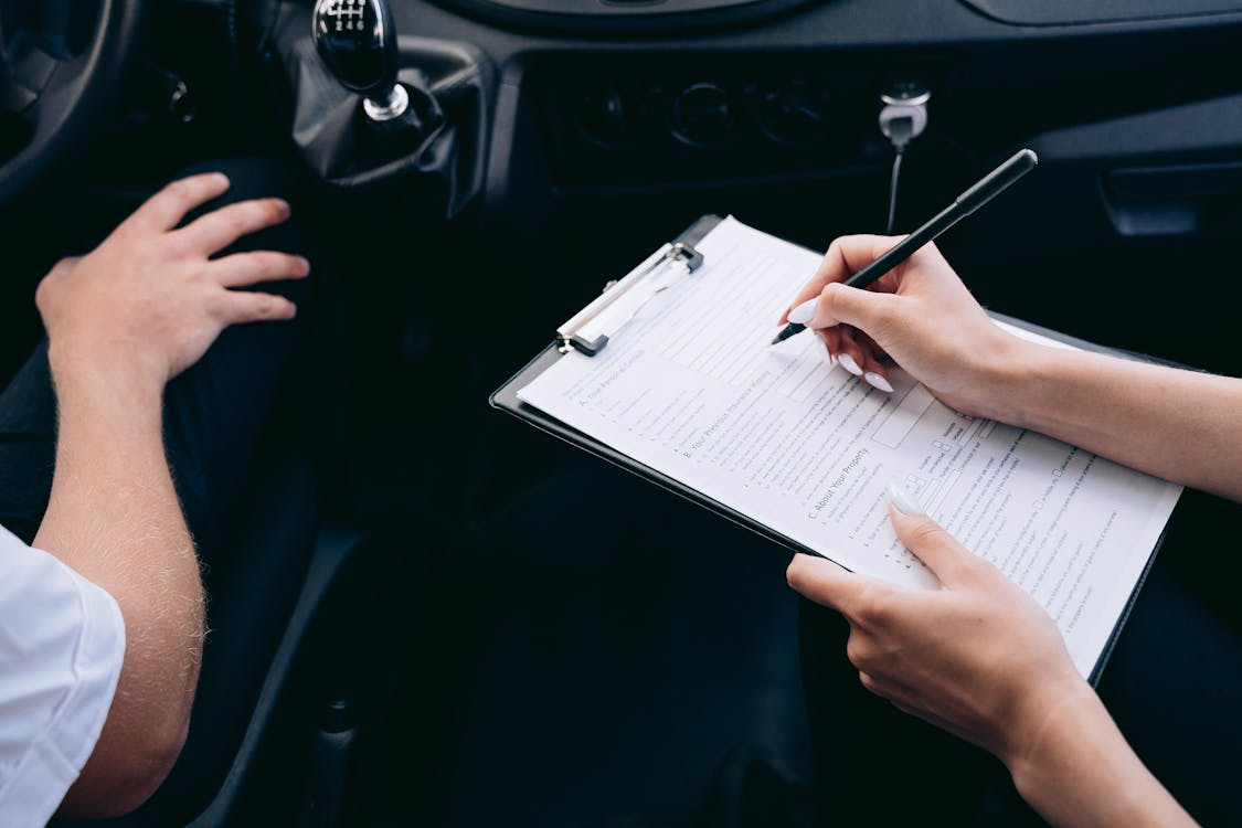 A person writing with a pen on a clipboard while seated inside a vehicle.