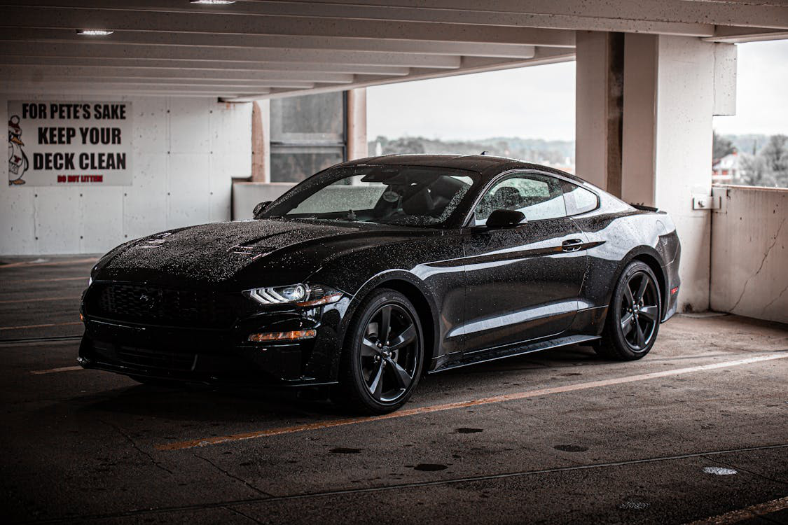 A black, shiny luxury car parked in a lot under sunlight.