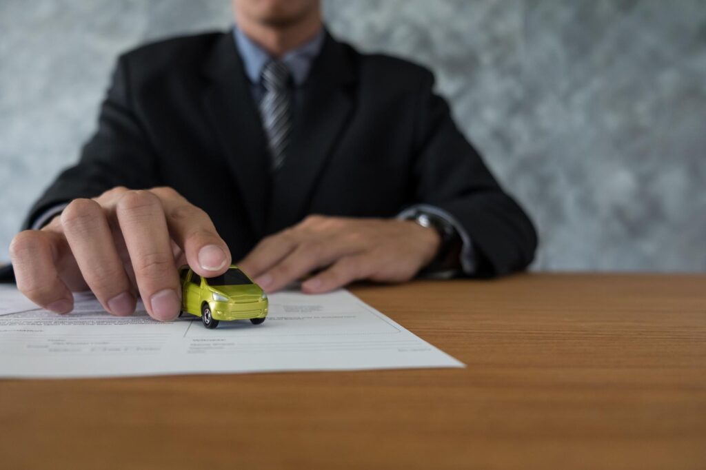 Man holding a miniature car on papers showing the risk of vehicle repossession after a missed
