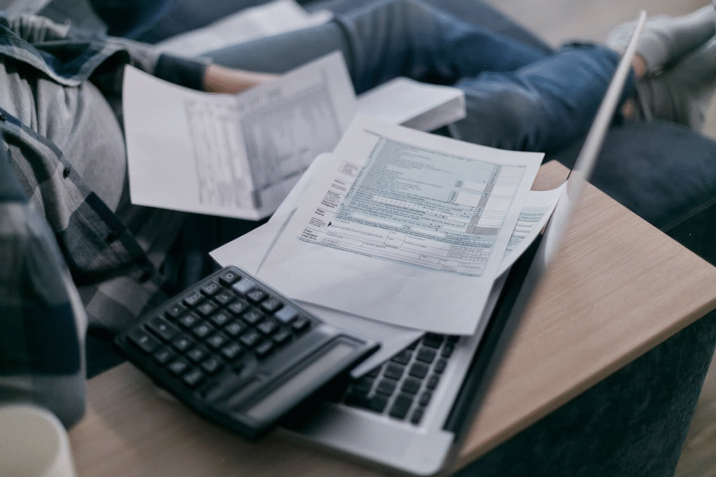 a person sitting with tax papers around a laptop and a calculator