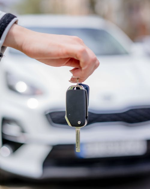 The image shows a person holding a car key in front of a white car.