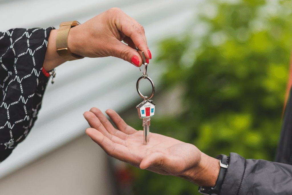 : Two people are shown exchanging a house key, with one hand giving the key and the other receiving it.