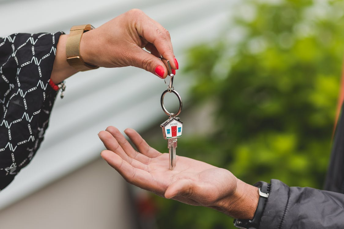 : Two people are shown exchanging a house key, with one hand giving the key and the other receiving it.