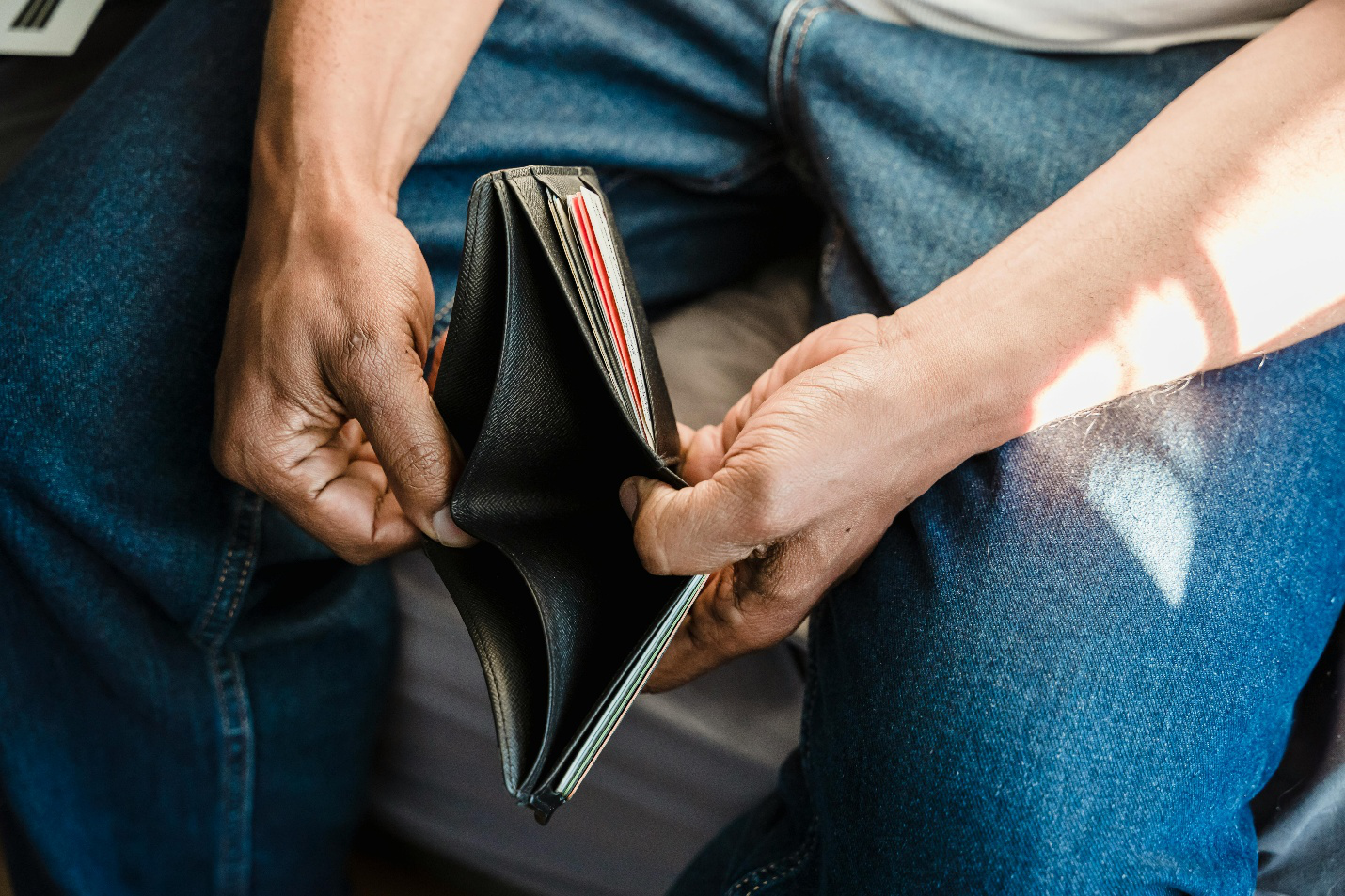 A person sitting down and holding an open empty wallet, showing financial hardship and stress