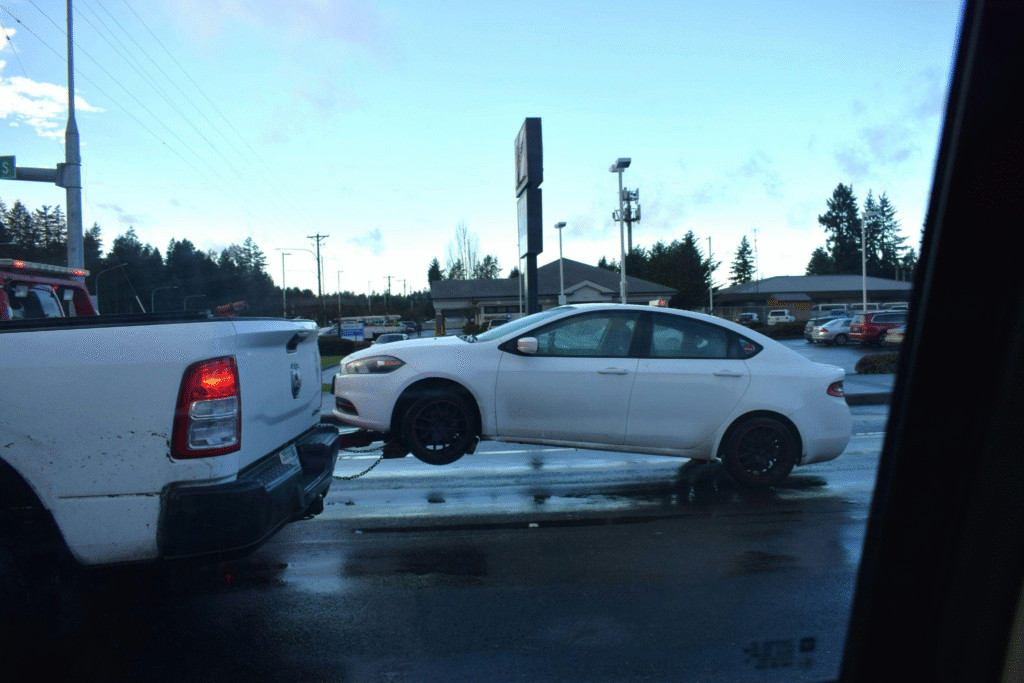 A white car being towed by a tow truck, due to a car repossession.