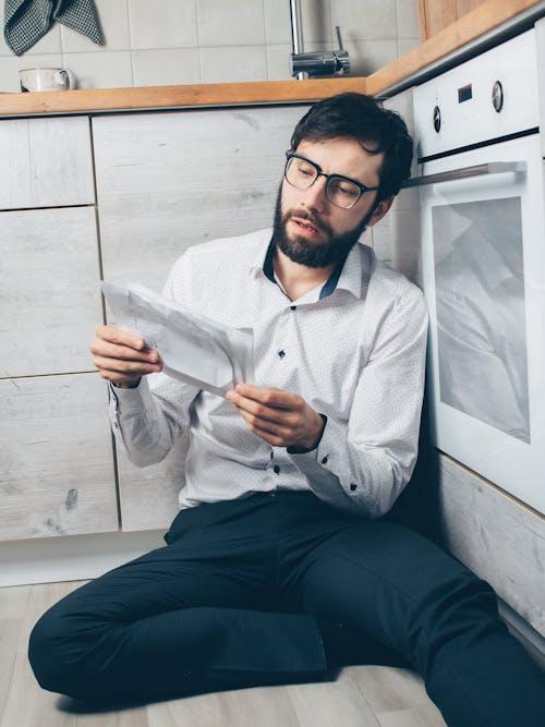 Stressed man sitting on the floor holding unpaid bills and financial notices