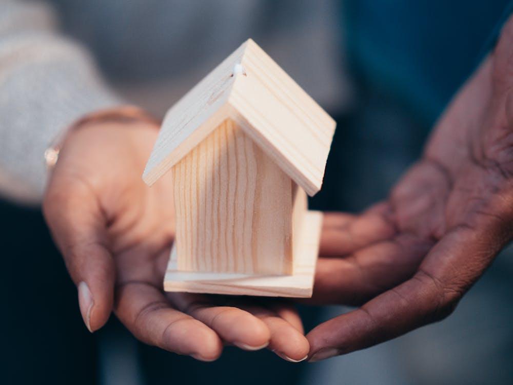 Hands gently holding a small wooden house model, symbolizing home, care, or real estate.