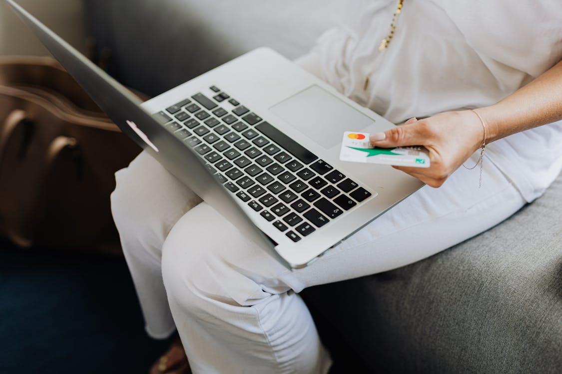  A person sits with a laptop on their lap while holding a credit card.
