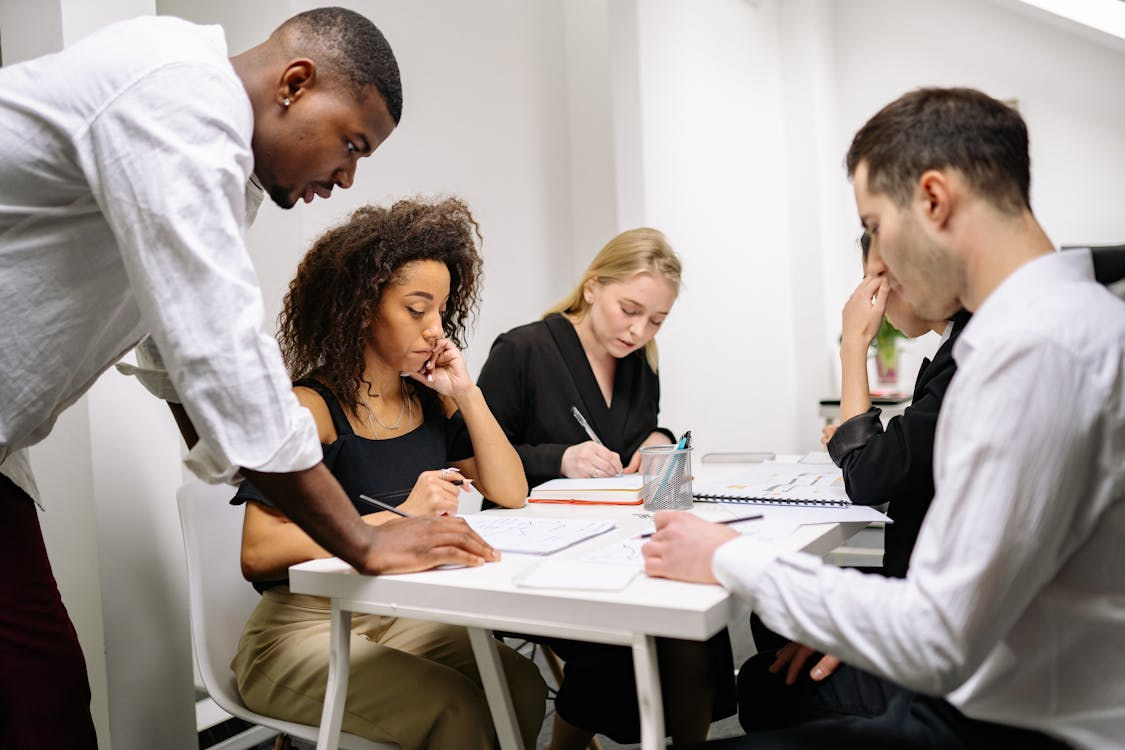 A group of professionals sits around a table, discussing documents and strategies, reflecting a business or legal meeting focused on debt resolution and legal guidance.