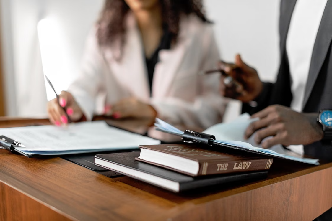 Two people reviewing legal papers on a clipboard beside law books on a wooden desk