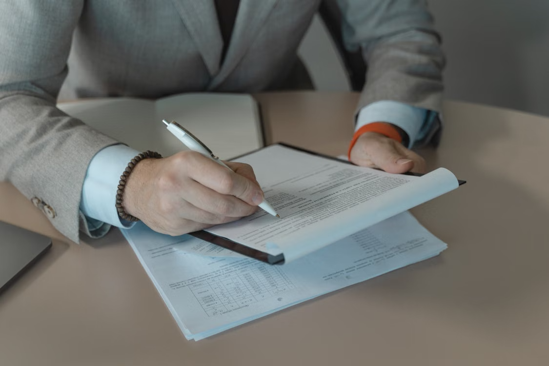Person in a gray suit writing notes on printed documents at a desk